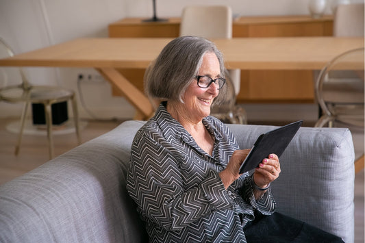 Picture of a woman wearing a black and white top sitting on the couch smiling and using a tablet.
