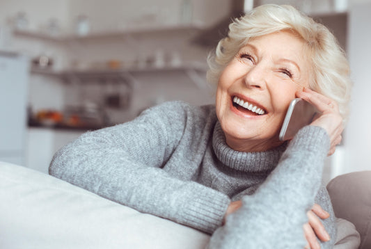 A happy senior citizen using a simply big phone, the BigPurplePhone. Wearing a grey sweater.