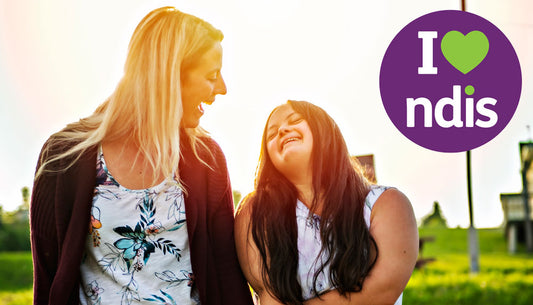 support worker and person smiling at each other in the sun with the NDIS logo to the top right corner of image.